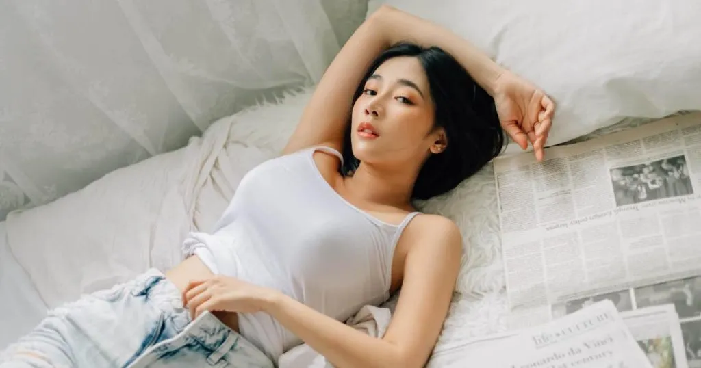Thai model Manow Bunnada laying down on a bed next to newspapers