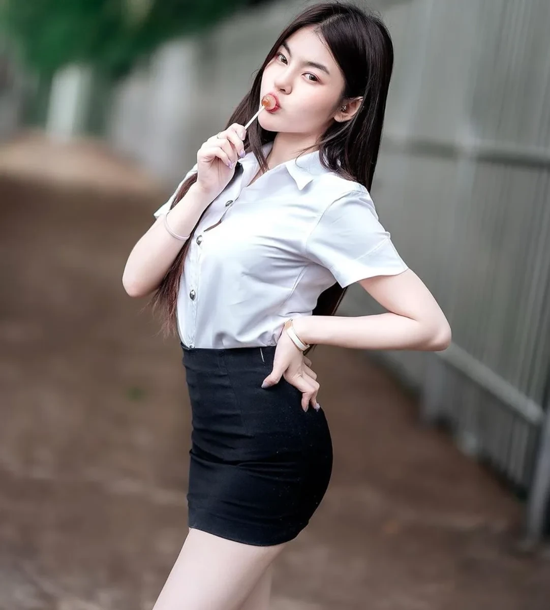 A playful student girl striking a pose with a lollipop, wearing a black skirt and a white top