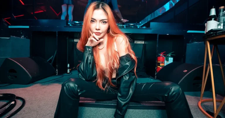 Thai girl DJ Riviere posing in a club with black outfit and red hair